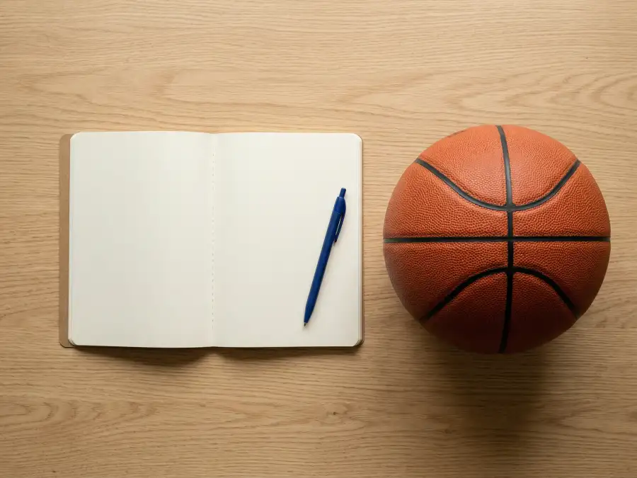 Aufgeschlagenes Notizbuch mit Stift und Basketball auf einem hellen Holztisch